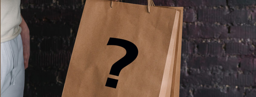 Kinsey Investigations Mystery Shopper Services - Two hands from two different people who are not pictured hold onto the handle of a brown shopping bag that is stamped with a large black question mark.