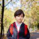 Kinsey Investigations Family Law Private Investigations Services - A school age boy is pictured walking along a tree-lined street and wearing a blue coat with a red zipper and a red backpack.