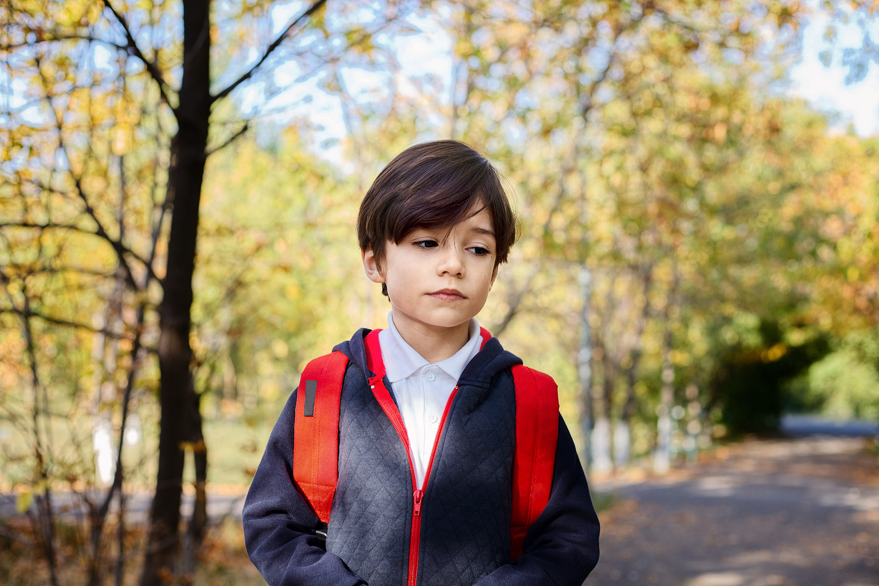 Kinsey Investigations Family Law Private Investigations Services - A school age boy is pictured walking along a tree-lined street and wearing a blue coat with a red zipper and a red backpack.