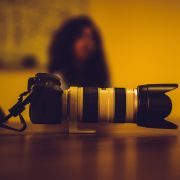 Kinsey Investigations offers Surveillance Services - A camera with a large telephoto lens is pictured in the foreground. A person with long dark hair sits in the blurred background