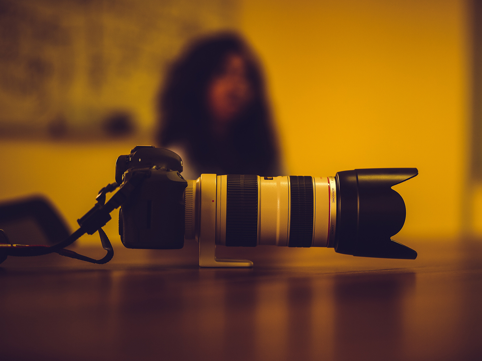 Kinsey Investigations offers Surveillance Services - A camera with a large telephoto lens is pictured in the foreground. A person with long dark hair sits in the blurred background