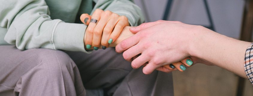 Kinsey Investigations Female Private Investigators offer tips for supporting someone in an abusive relationship - Someone with long hair and painted nails sits with their hands in their lap. Someone not pictured is holding one of their hands.