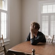 KinseyInvestigations.com Infidelity Investigations - A person sits at a kitchen table with their head in their hands.