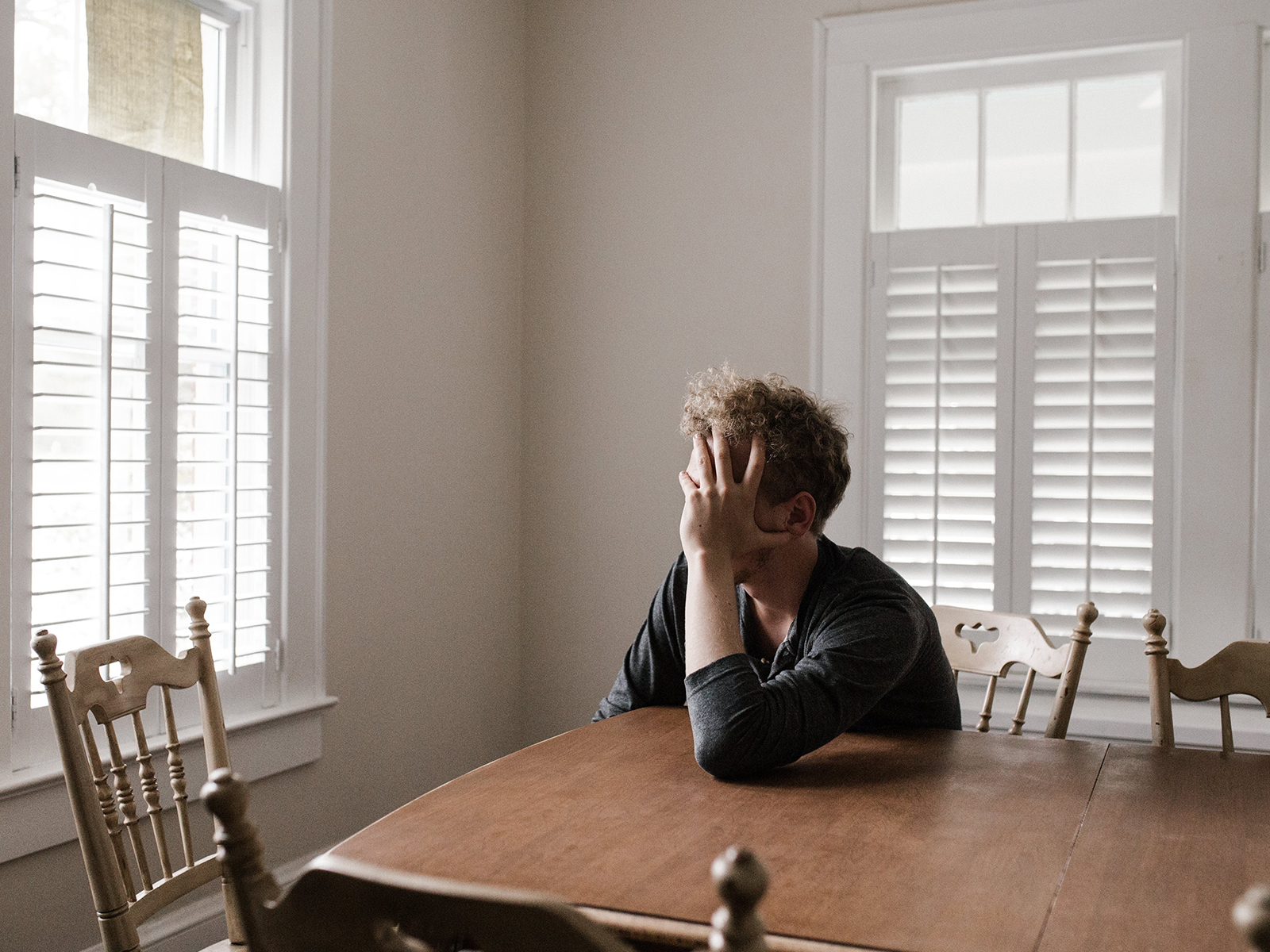 KinseyInvestigations.com Infidelity Investigations - A person sits at a kitchen table with their head in their hands.