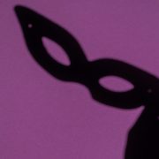 KinseyInvestigations.com Background Check Screenings - The shadow of a theatrical face mask is cast on a purple background.
