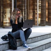 KinseyInvestigations.com Becoming a Private Investigator - A woman using a cell phone and laptop sits on steps in front of a building.