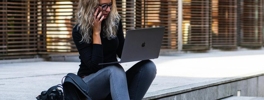 KinseyInvestigations.com Becoming a Private Investigator - A woman using a cell phone and laptop sits on steps in front of a building.