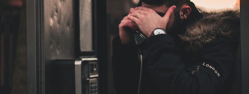 Kinsey Investigations Hire an Investigator to Find Someone - A man using a payphone conceals his face with his hand.