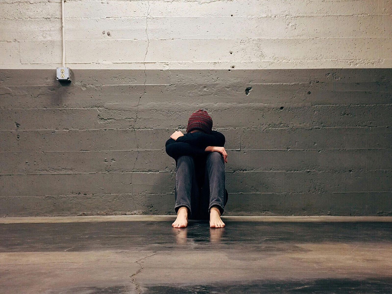 KinseyInvestigations.com Missing Person in L.A. - A barefoot person sits on the ground with their back to a cinder block wall.