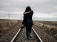 KinseyInvestigations.com Finding Missing Persons - A woman wearing a long jacket walks on a railroad track in a deserted landscape.