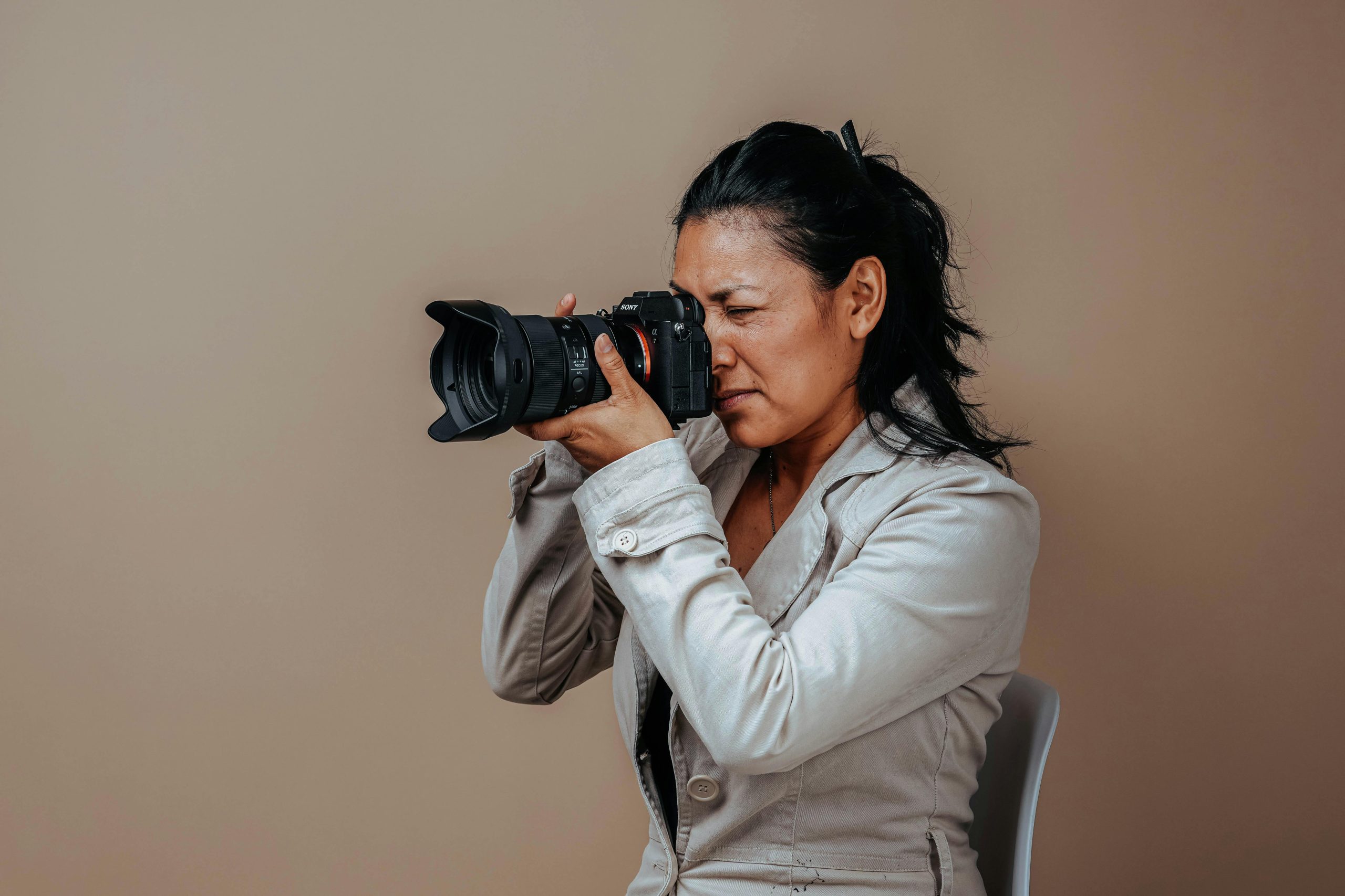 Woman in gray suit holding DSLR camera to her eye - Visit KinseyInvestigations.com.