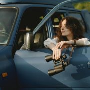 Female private detective in car window holding binoculars - Consult Kinsey Investigations.