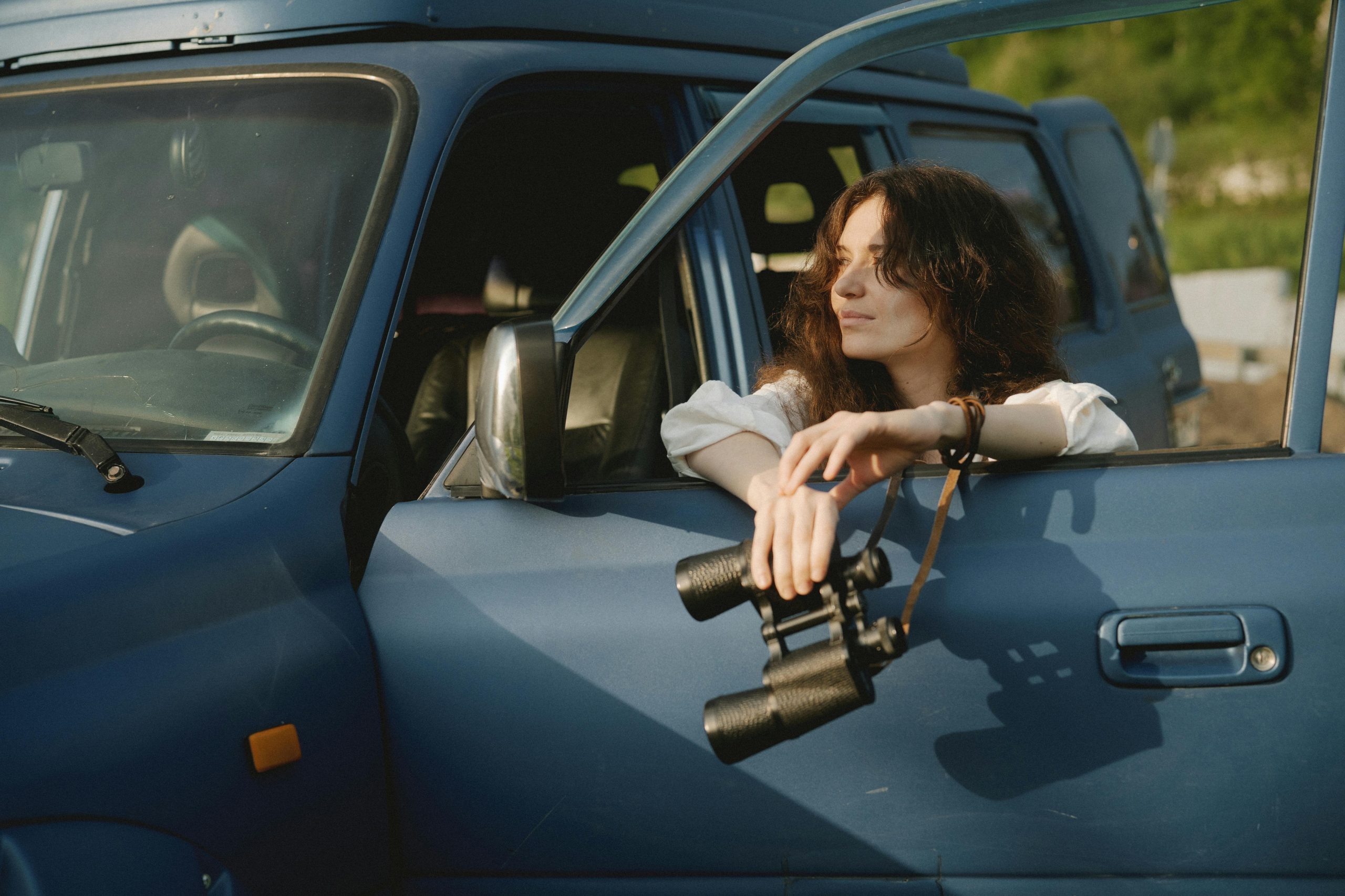 Female private detective in car window holding binoculars - Consult Kinsey Investigations.