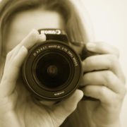 Sepia-toned image of a female detective with a camera in front of her face - Consult Kinsey Investigations.