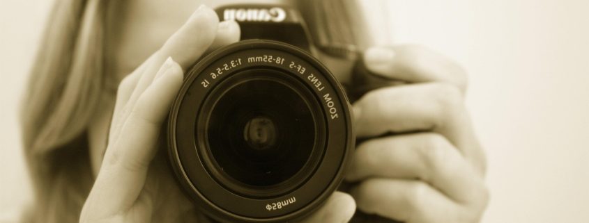 Sepia-toned image of a female detective with a camera in front of her face - Consult Kinsey Investigations.